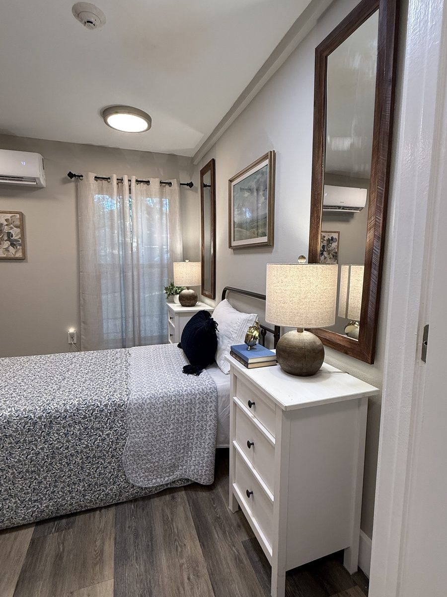 A resident room with white nightstands, linen lamps and a framed landscape painting